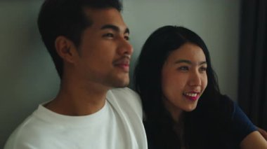Happy young asian boyfriend and girlfriend having a conversation while sitting close together at home