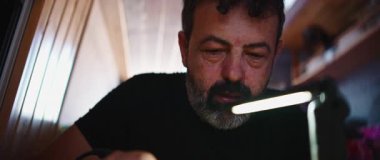 Electronics technician meticulously soldering a microchip, illuminated by a desk lamp