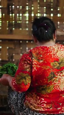 Geleneksel lahu kadını ateşten kaynamış çay yapraklarını ayıklıyor ve kurutmak için hasır bir tepsiye koyuyor.