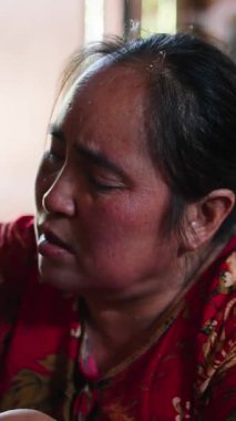 Güneydoğu Asyalı bir kadın yerde yemek pişirirken, bir erkek sakince çıplak ayakla sigara içiyor.