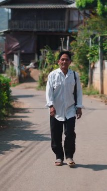 Güneydoğu Asyalı olgun bir adam köy ağaçları arasında asfalt köy yolunda yürüyor - FullHD Dikey