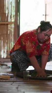 Deneyimli Asyalı kadın ateşin yanındaki hasır tepside kaynamış çay yapraklarını kurutuyor.