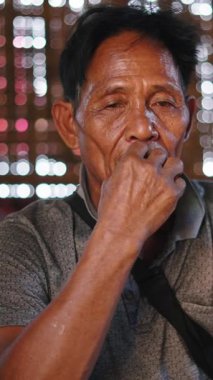 Asyalı olgun bir adam bambu ve ahşap bir evde geleneksel bir sigara içerken derin derin oturup düşünür.