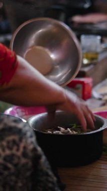 Geleneksel lahu kıyafetleri giymiş bir kadın, içindekileri tabakta FullHD dikey olarak otururken eliyle karıştırıyor.