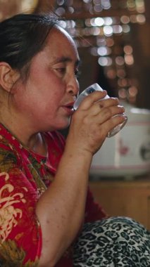 Lahu kadını geleneksel ahşap ve kamış kulübesinde kristal bardaktan sıcak çay içiyor.