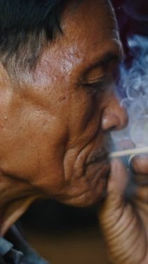 Yakın plan Asyalı adam lahu sakin ve rahat son sınıf öğrencisi el yapımı sigarayı geleneksel bir şekilde yakıyor.