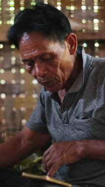 İhtiyar lahu, bambu kulübesinin zemininde oturan akıllı telefon ekranına danışarak sakince pirinç yiyor.