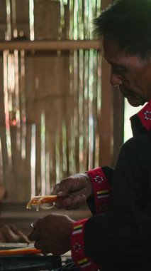 Olgun bir Asyalı adam bambu duvarlı bir kulübede geleneksel yöntemlerle ateş yakıyor.