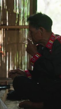 Lahu kabilesinden bir Asyalı, bambu duvarlı geleneksel bir kulübede yemek hazırlarken sigara içiyor.