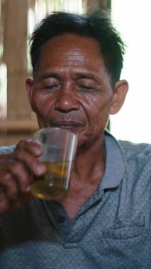 Geleneksel bir ahşap evde oturan Asyalı Lahu Yaşlısı Bir yandan sigara içerken diğer yandan çay içiyor - FullHD Dikey