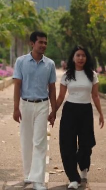 Mutlu genç sevgili ve kız arkadaş, güneşli bir günde yeşil bir parkta romantik bir yürüyüş yapıyorlar.