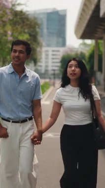 Genç mutlu Asyalı çift, romantik bir randevu sırasında el ele tutuşup bir şehir caddesinde yürüyorlar.