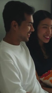 Sevecen genç Asyalı çift kanepede oturuyor, konuşuyor, gülümsüyor ve birlikte vakit geçiriyorlar.