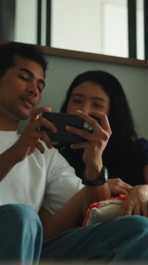 Asyalı çift evdeki kanepede oturuyor, sosyal medyada geziniyor ya da cep telefonuyla film izliyor.