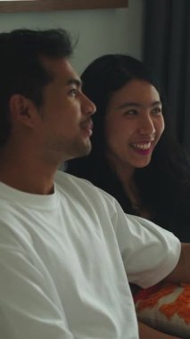 Asyalı çift TV 'de film izliyor, gülüyor ve evdeki kanepede birlikte eğleniyorlar.