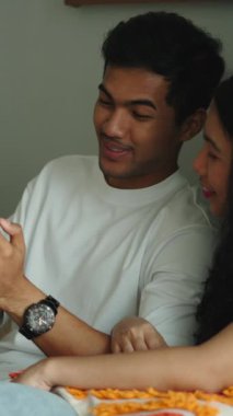 Sevecen Asyalı çift kanepede dinleniyor ve cep telefonunda birlikte dolaşıyorlar.