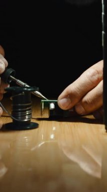 Elektronik bileşenleri lehimleyen yetenekli teknisyen, hassas onarımlar sırasında yakınlarda dinlenen tel makara.