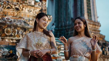 Geleneksel kıyafetler giyen iki gülen Taylandlı kadın aydınlanmış Wat Arun tapınağının önünde dikiliyorlar.