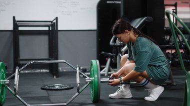 Genç bir kadın antrenman için ağır büyü çubuğu kuruyor. Spor salonundaki antrenmanına odaklanıyor.