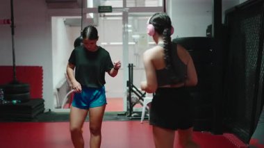 İki atletik kadın dövüş sporları salonunda ısınma egzersizleri ve ayak egzersizleri yapıyor.