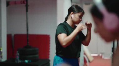 Spor salonunda antrenman yaparken Muay Thai kombinasyonları ve savunma hareketleri üzerinde çalışan odaklanmış genç bir kadın.