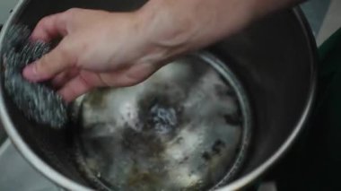 Profesyonel mutfak işçisi büyük paslanmaz çelik bir tencereyi metal bir süngerle yıkıyor. 4K yatay.