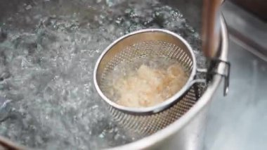 Sıcak su dolu paslanmaz çelik bir tencerede metal bir süzgeçte makarna kaynıyor. 4K yatay.