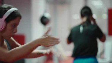 Kulaklık takan kararlı bir bayan sporcu dövüş sanatları tekniğini dövüş salonunda uyguluyor.