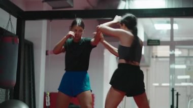 Modern bir spor salonunda dövüş teknikleri ve gölge boksu yapan iki genç kadın.
