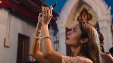 Bangkok 'taki Wat Arun Tapınağı' ndaki Loi Krathong festivalini yakalamak için akıllı telefon kullanan genç bir kadın.