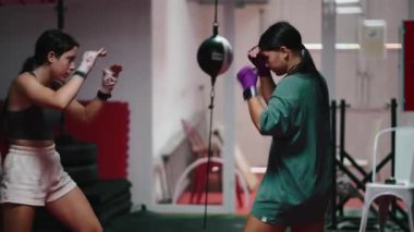 Dövüş sporları kulübünde kickboks, yumruk, tekme ve kaçınma pratiği yapan iki atletik kadın - 4K yatay