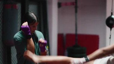 Dövüş yeteneklerini geliştirmek için motive olmuş iki bayan sporcu, spor salonunda yumruk ve tekmelerle antrenman yapıyorlar - 4K yatay.