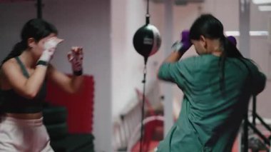 Dövüş kulübünde antrenman yaparken boks teknikleri uygulayan ve antrenman yapan iki genç kadın - 4K yatay.