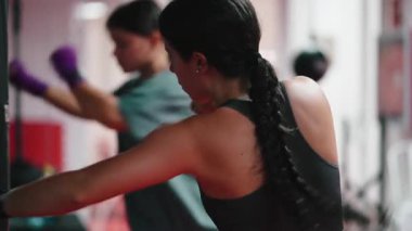 İki motive olmuş bayan sporcu boks antrenmanı sırasında kum torbaları üzerinde boks yapıyor. 4K yatay.