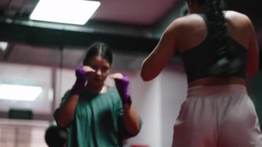 İki genç kadın heyecanlı bir boks antrenmanı yapıyor, yumruklaşıyorlar ve savunma hareketleri yapıyorlar - 4K yatay.