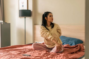 Genç bir kadın yatakta gövdesini geriyor, evde dikkatli bir sabah rutini uyguluyor.