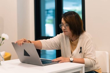 Kadın dizüstü bilgisayar açıyor, çalışmaya ya da çalışmaya hazırlanıyor, siyah bir kurdele takıyor.