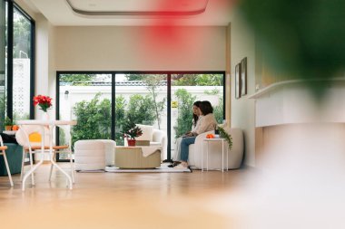 Işıl ışıl aydınlık, geniş pencereli çağdaş yaşam alanında beyaz bir kanepede dinlenen iki kadın.