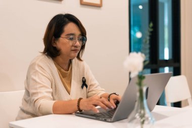 Dizüstü bilgisayarda yazan, siyah kurdele takan, yas tutan, hatırlayan ya da dayanışmayı simgeleyen bir kadın.