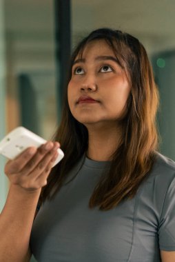 Beyaz bir uzaktan kumanda kullanan genç bir kadın, bir aygıt veya ayarları yönetmek için yukarı bakıyor