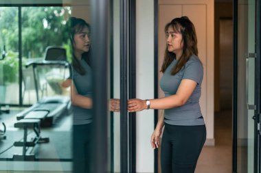 Kadın antrenmana hazırlanıyor, modern spor salonunun kapısını açıyor kararlılığı yansıtıyor