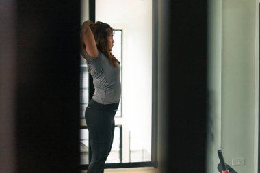 Kadın içeride esneme egzersizleri yapıyor, ev antrenmanına hazırlanıyor.