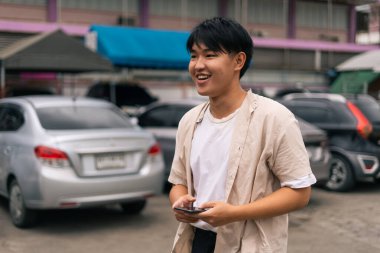 Meşgul bir caddede elinde cep telefonuyla dikilirken Asyalı adam gülümsüyor ve başka tarafa bakıyordu.