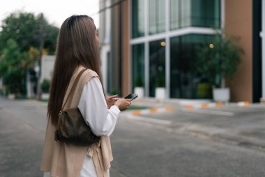 Dışarıda yürüyen ve cep telefonu kullanan genç bir kadın, şehir ortamında geziniyor.