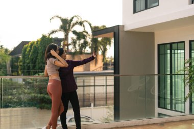 Kadınlar modern bir balkonda selfie çekiyorlar, akıllı telefonlarıyla sosyal anları yakalıyorlar.