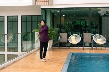 Modern bir güvertede, yüzme havuzunun yanında hafif hareketler yapan bir kadın, sağlığını arttırıyor.