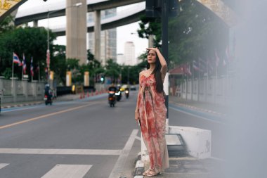 Yoğun bir caddede dikilen kadın, gözlerini güneş ışığından ayırmıyor, önüne bakıyor, şehir yaşamında yön arıyor.