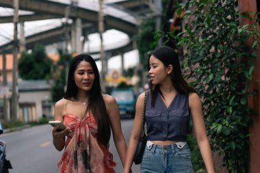 İki Asyalı genç bayan arkadaş birlikte vakit geçiriyorlar, bir şehir caddesinde el ele dolaşıyorlar
