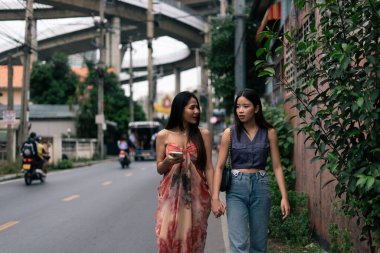 İki Asyalı kadın arkadaş el ele yürüyorlar, şehir caddesinde sohbet ediyorlar.