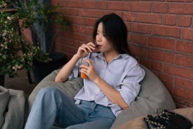 Genç Taylandlı kadın buzlu çay içiyor, rahat bir şehir kafesinde rahatlatıcı bir anı yakalıyor.